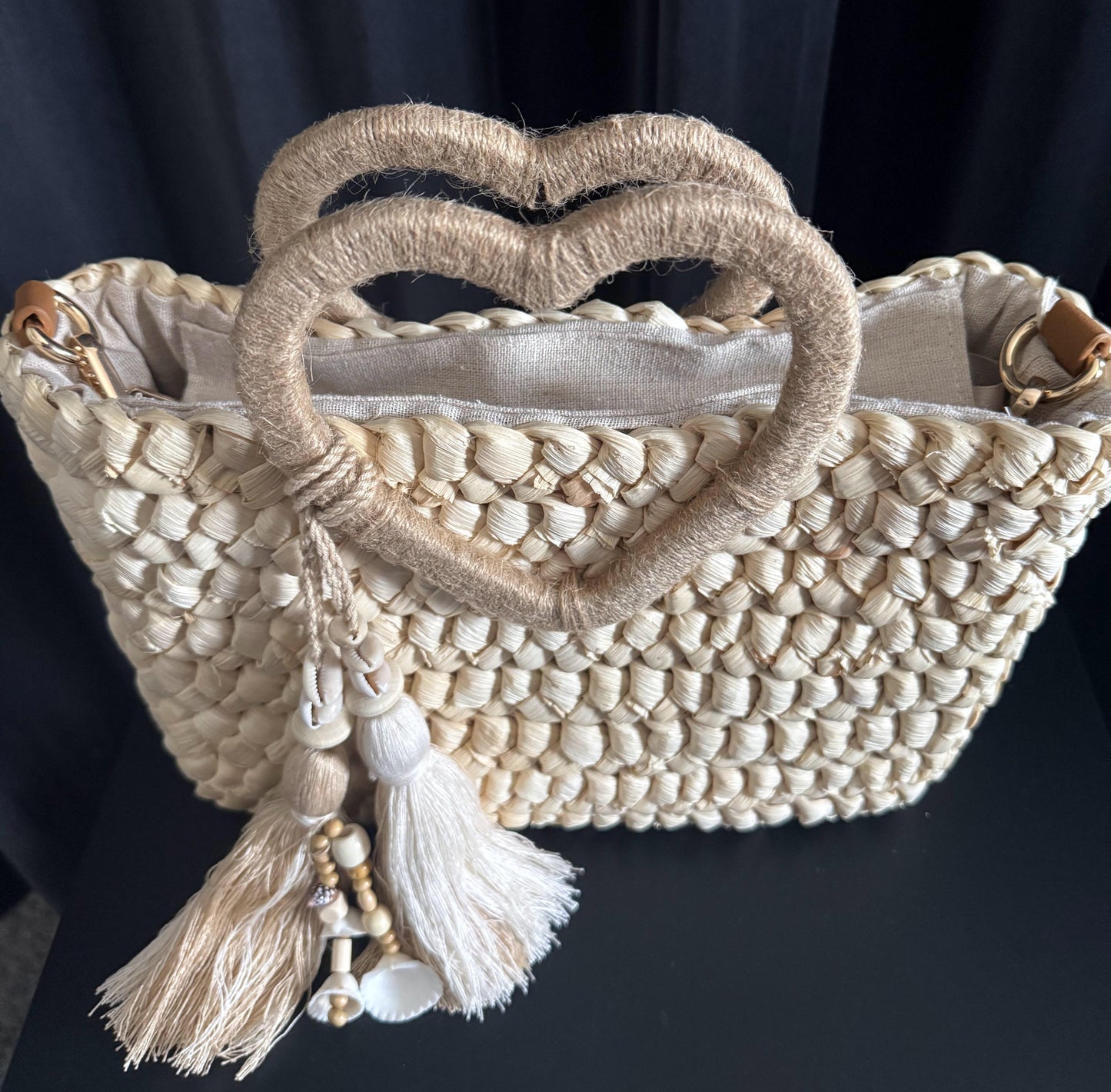 Capazo trenzado con asa en forma de corazón y detalles boho, perfecto para un estilo romántico y veraniego