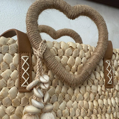 Capazo trenzado con asa en forma de corazón y detalles boho, perfecto para un estilo romántico y veraniego.