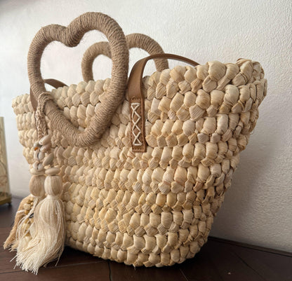 Capazo trenzado con asa en forma de corazón y detalles boho, perfecto para un estilo romántico y veraniego.