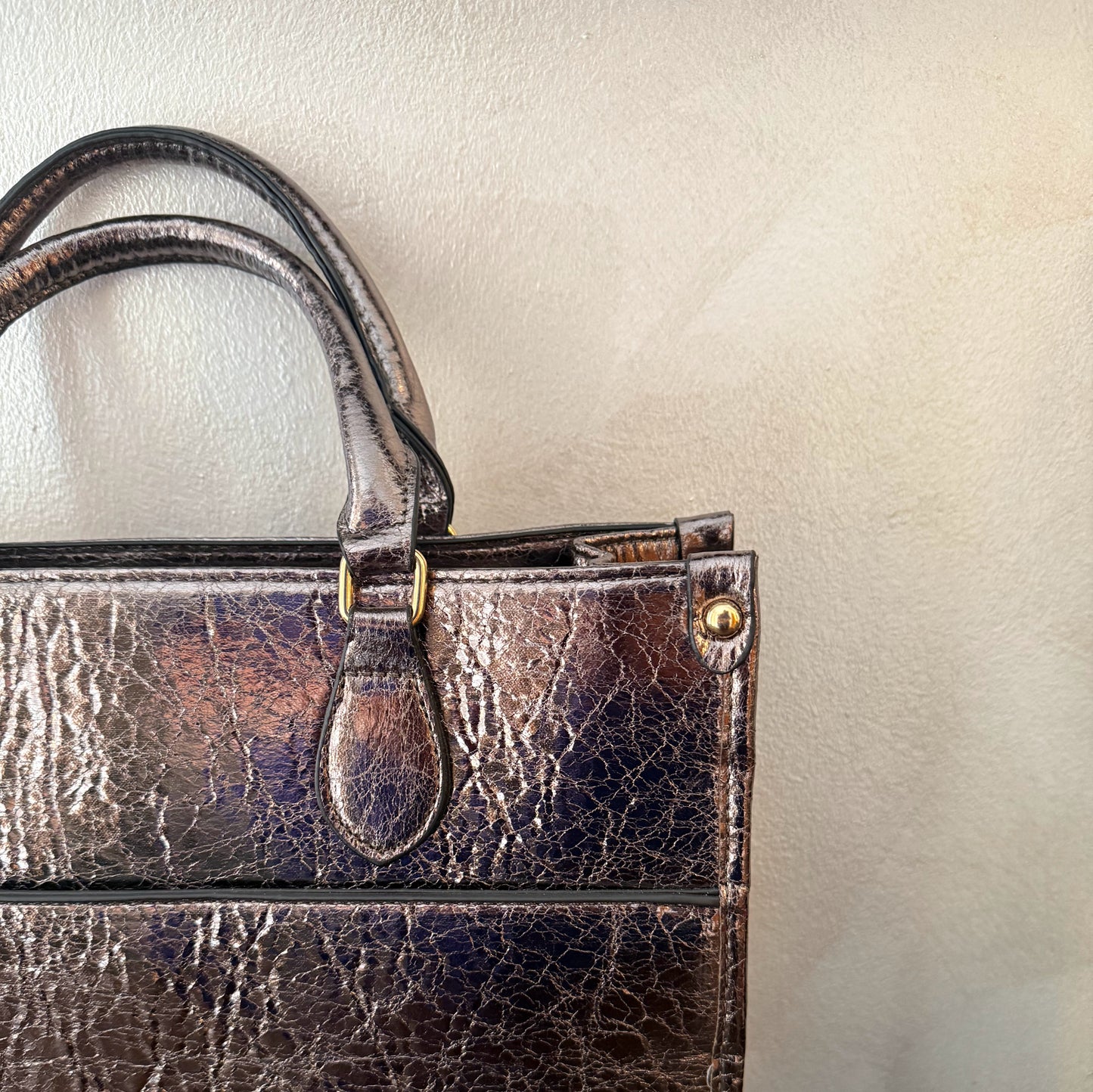 Cartera metalizada con con asa de mano y asa larga.