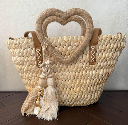 Capazo trenzado con asa en forma de corazón y detalles boho, perfecto para un estilo romántico y veraniego.