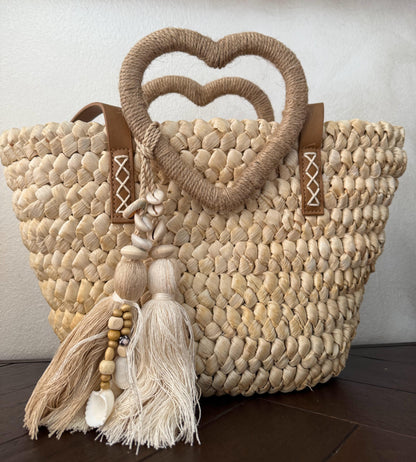 Capazo trenzado con asa en forma de corazón y detalles boho, perfecto para un estilo romántico y veraniego.