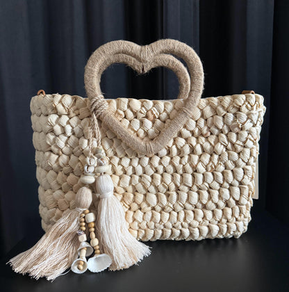 Capazo trenzado con asa en forma de corazón y detalles boho, perfecto para un estilo romántico y veraniego