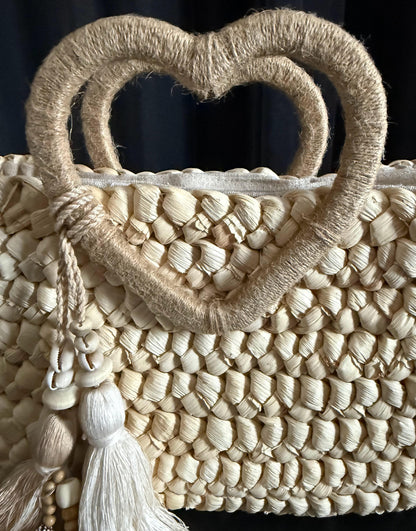 Capazo trenzado con asa en forma de corazón y detalles boho, perfecto para un estilo romántico y veraniego