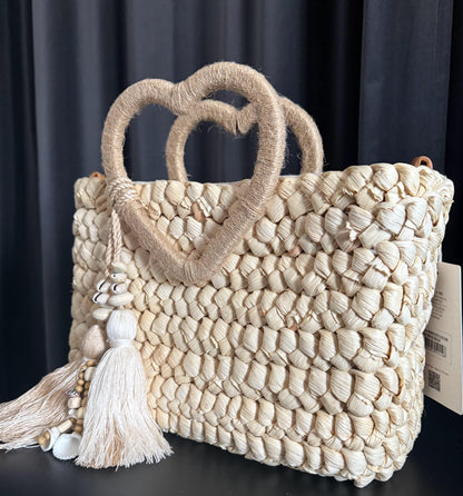Capazo trenzado con asa en forma de corazón y detalles boho, perfecto para un estilo romántico y veraniego